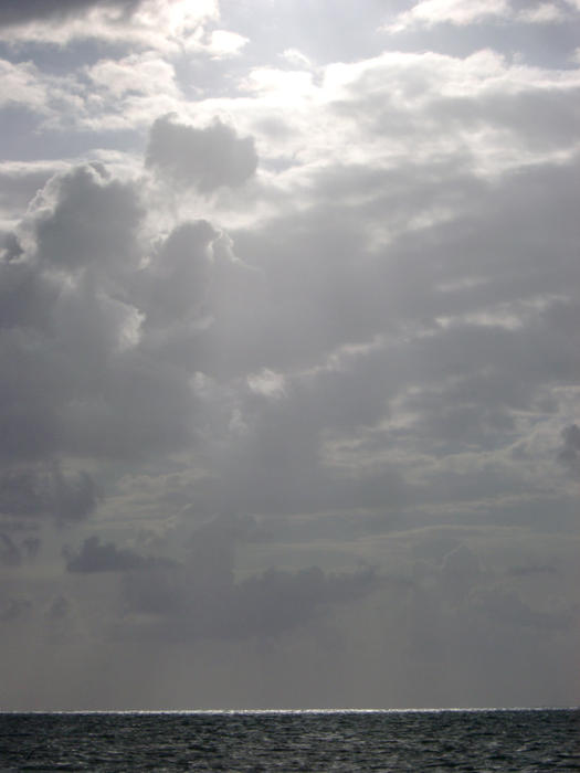 sun casting a beam of light onto the water from a storm sky