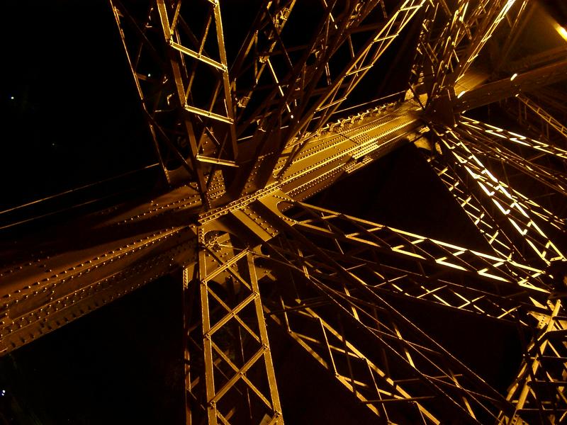 inside the metal structure of the eiffel tower, flood lit at night
