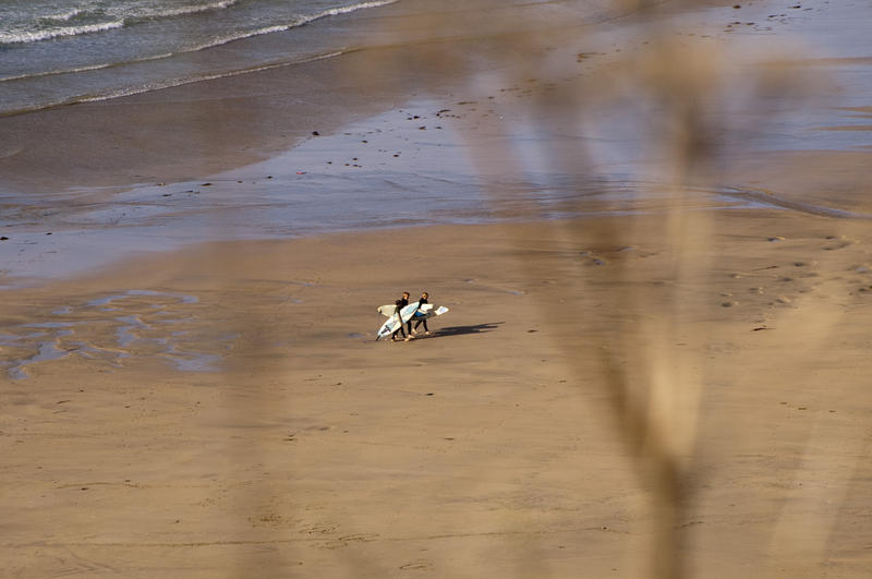 looking down at an empty beach with a couple of surfers retruning from an afternoon surf