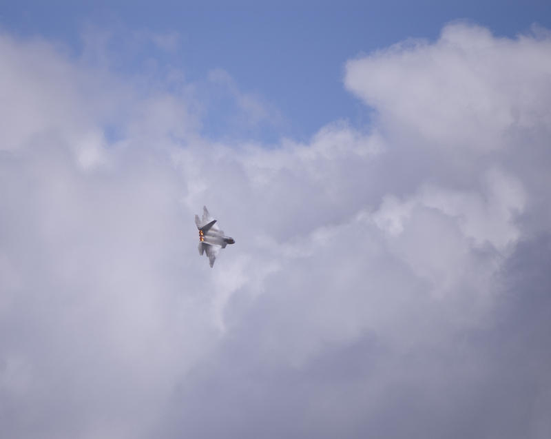 an F-22 making a tight turn at an airshow with afterburner engines glowing