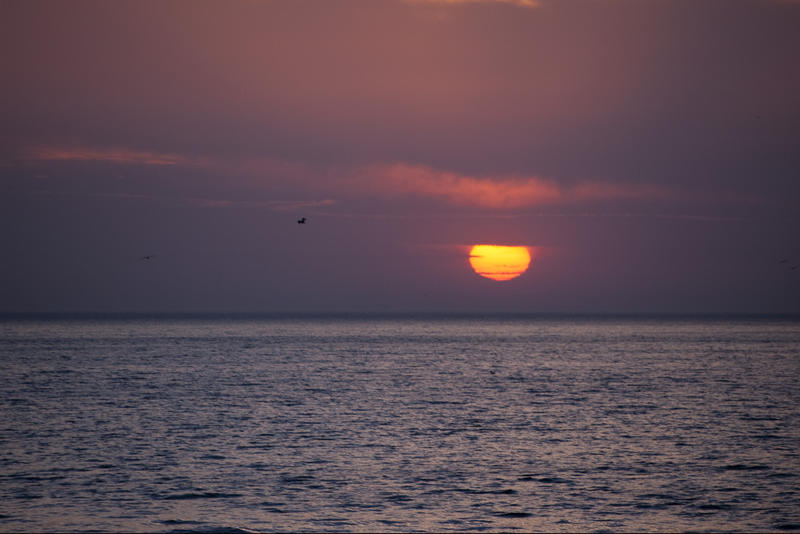 an orange red glowing sunset with layers of cloud over the ocean