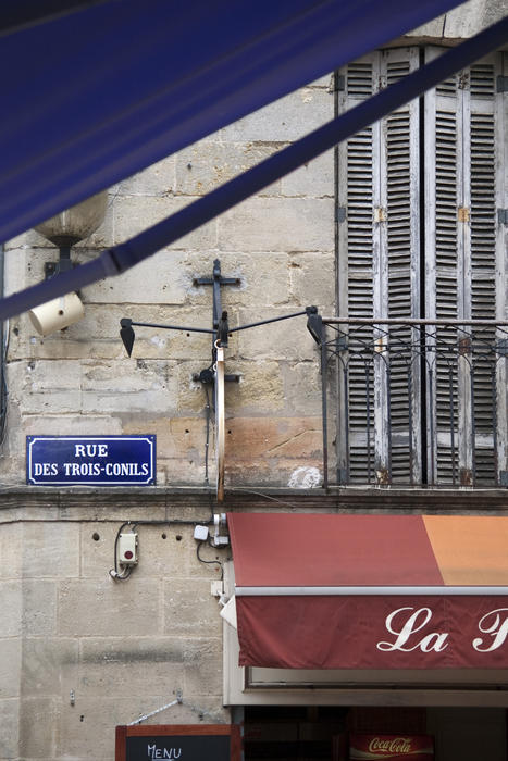 details of a french town street, blue enamel street sign, cafe awning, and shuttered windows