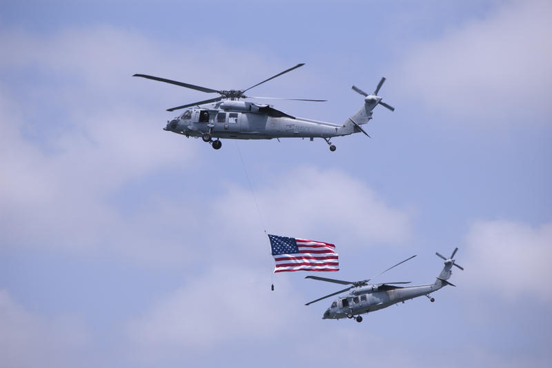 a helicopter airshow display with one helicopter flying the american flag