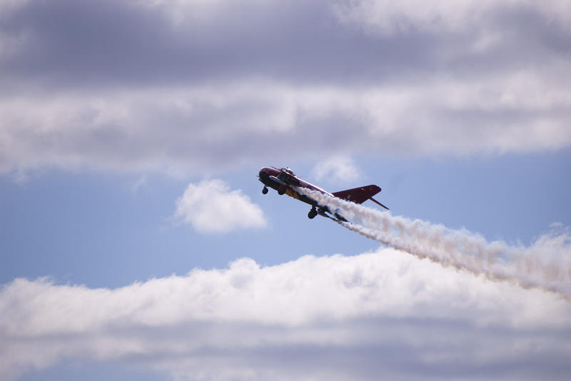 a restored mig 17 fighter plane in flight with a trail of smoke