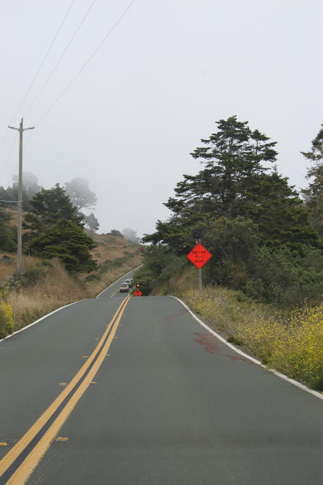 a bright orange warning sign for a single lane road ahead