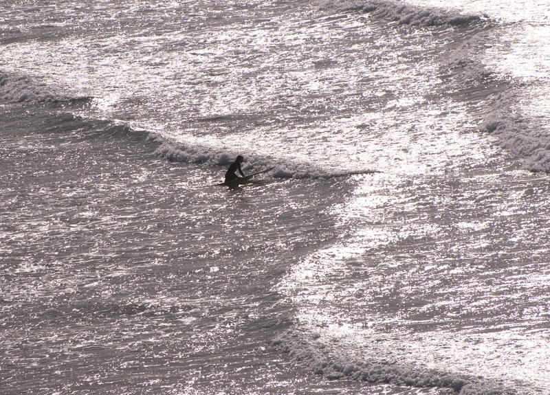 a contre-jour image of a surfer paddling out through the breaking surf