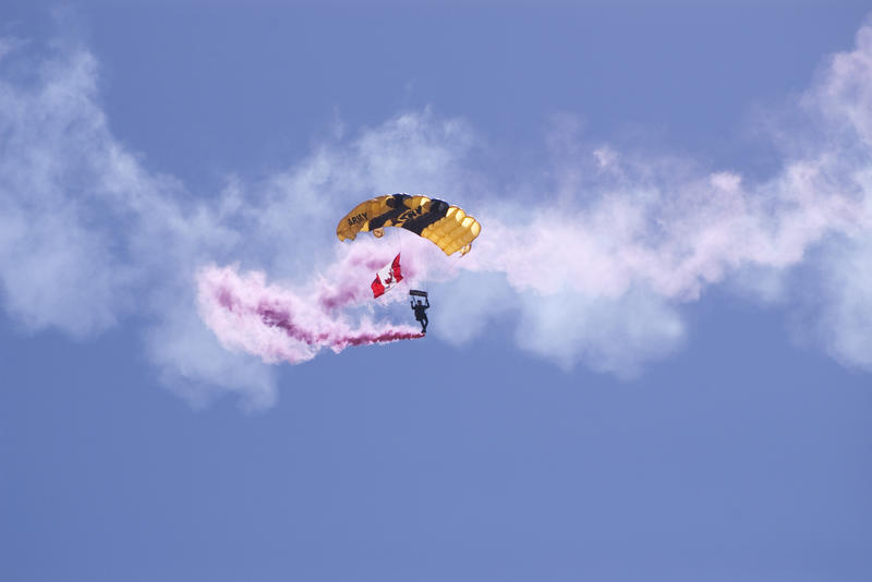 a canadian army parachutist gliding down with a trail of pink smoke