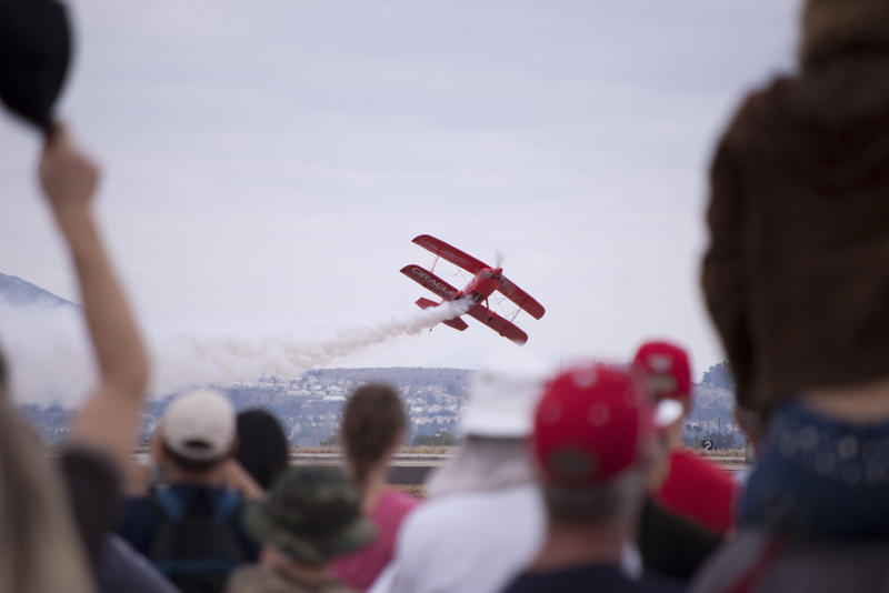 the crowd watches a red stunt plane at an airshow