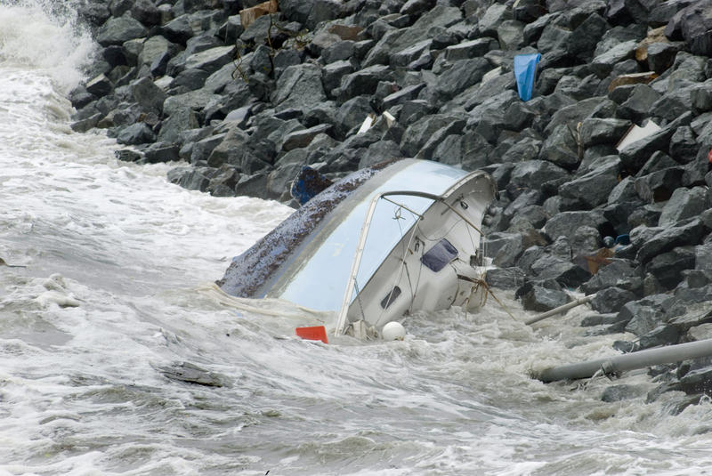 a sailing yacht wrecked by waves smashing it against a rock wall