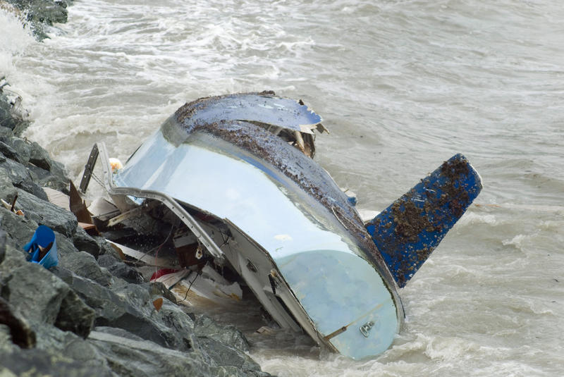 a sailing yacht wrecked by waves smashing it against a rock wall