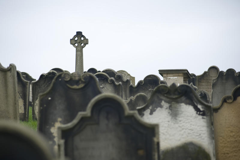 rows of grave stones with a celtic cross memorial in the distance