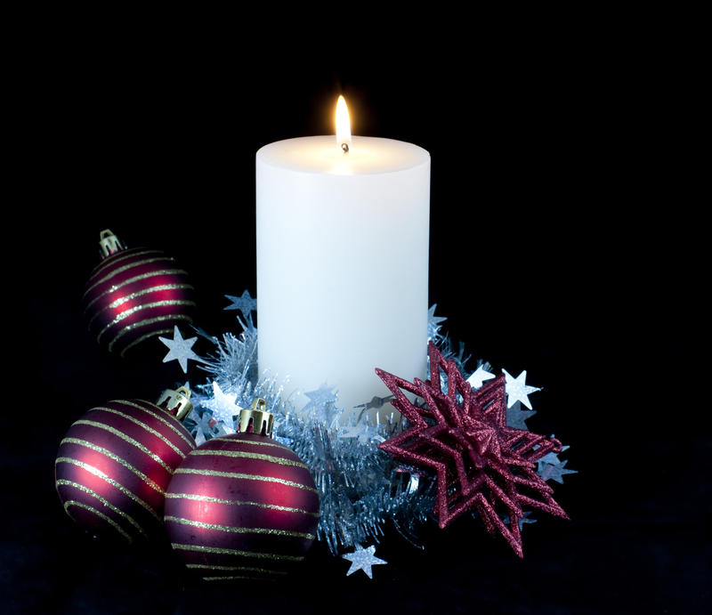 a white candle decorated with christmas balls and tinsel