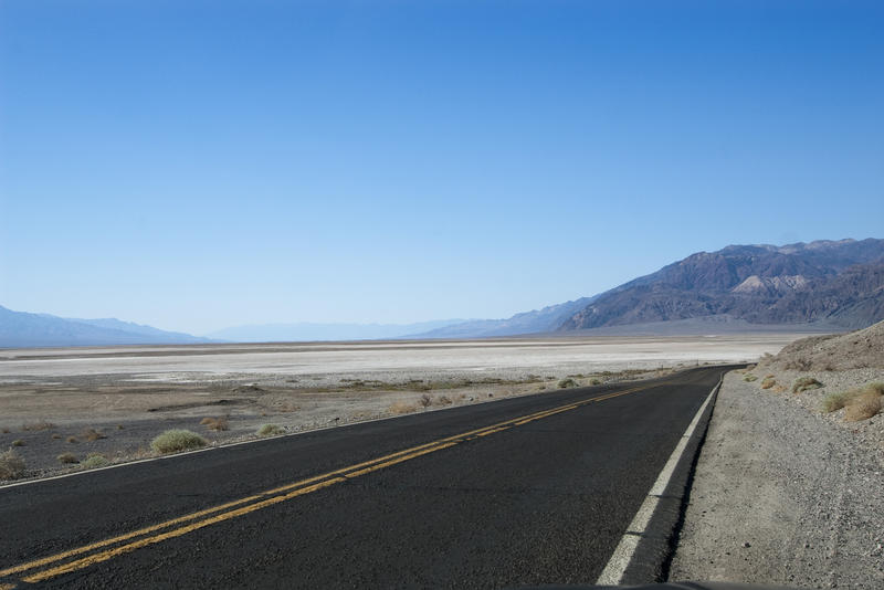 a long empty desert road thrugh a featureless landscape in death valley