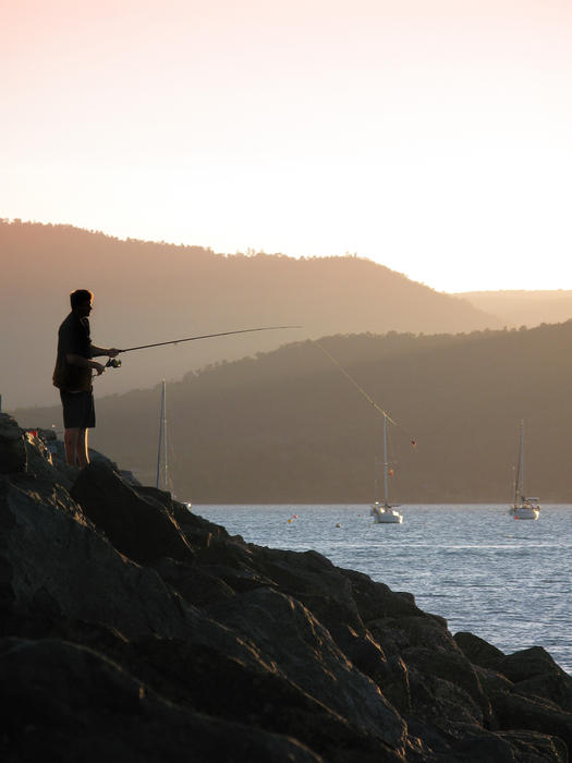 a standing on a rock wall fishing at sunset