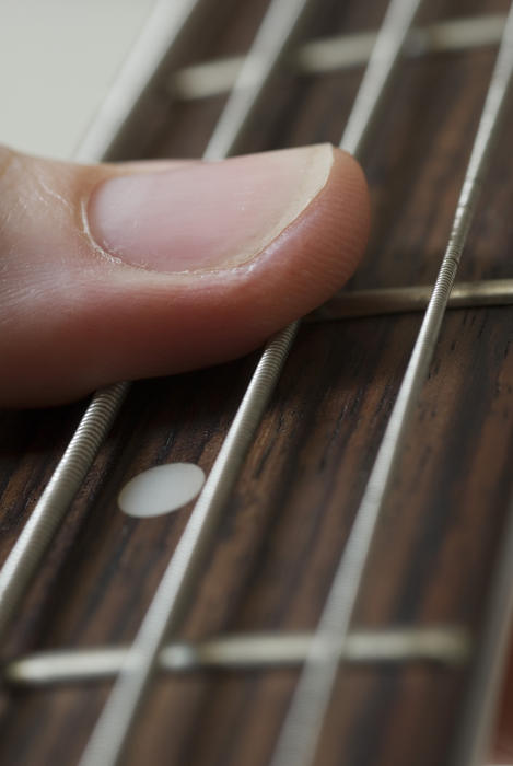 a finger holding strings on a bass guitar