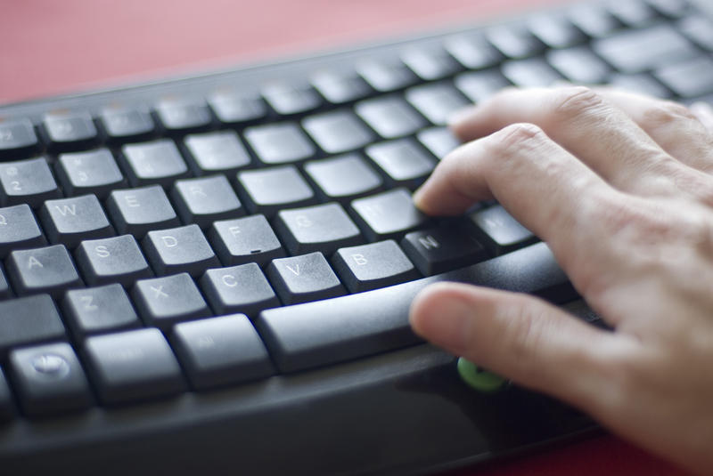 a hand typing on a black keyboard with a red backdrop