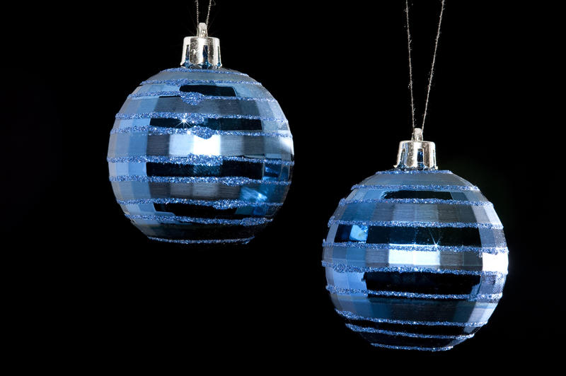 two metallic blue christmas baubles hanging in front of a black background