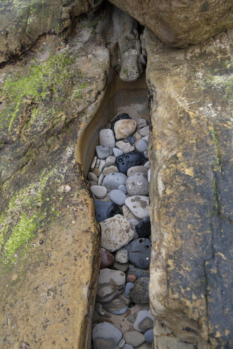 a hollow in rocks on the seashore with rounded sea washed pebbles inside