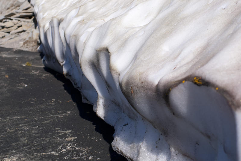 snow melted back by sun heatnig a near-by black stone surface 