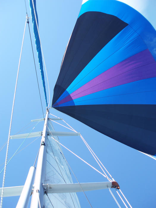 looking up at a yacht mast with its colorful spinnaker catching the wind