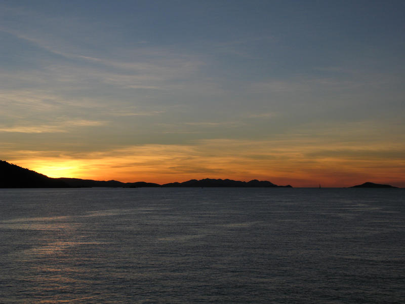 a panoramic image of the sun setting over the ocean with the silhouette of a distant peninsula