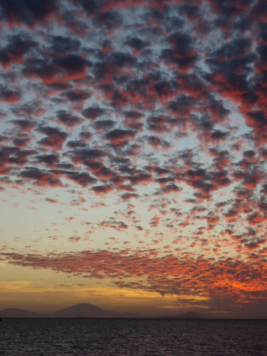 glowing sunset clouds and distant land across the water and the end of the day