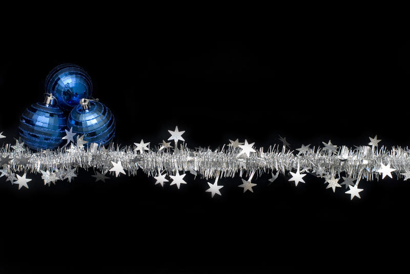 a string of silver tinsel with three red christmas balls on a black background