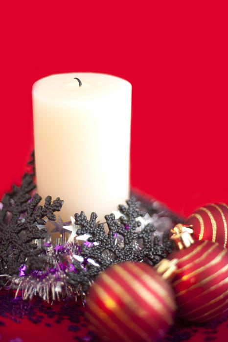 a still life of an unlit christmas candle and decorations on a bright red backdrop