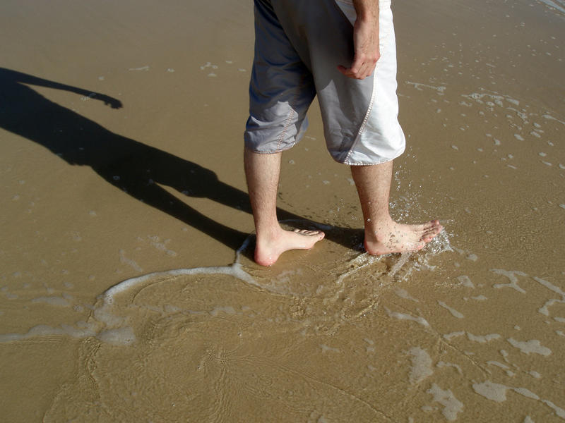 a man walking along the beach though shallow breaking waves