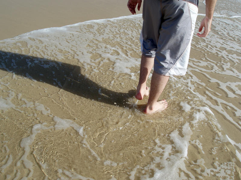a man walking along a sandy shore through shallow breaking waves