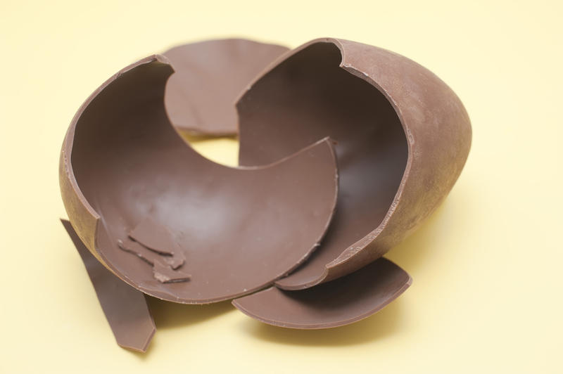 Closeup of broken chocolate Easter Egg fragments lying on a yellow background