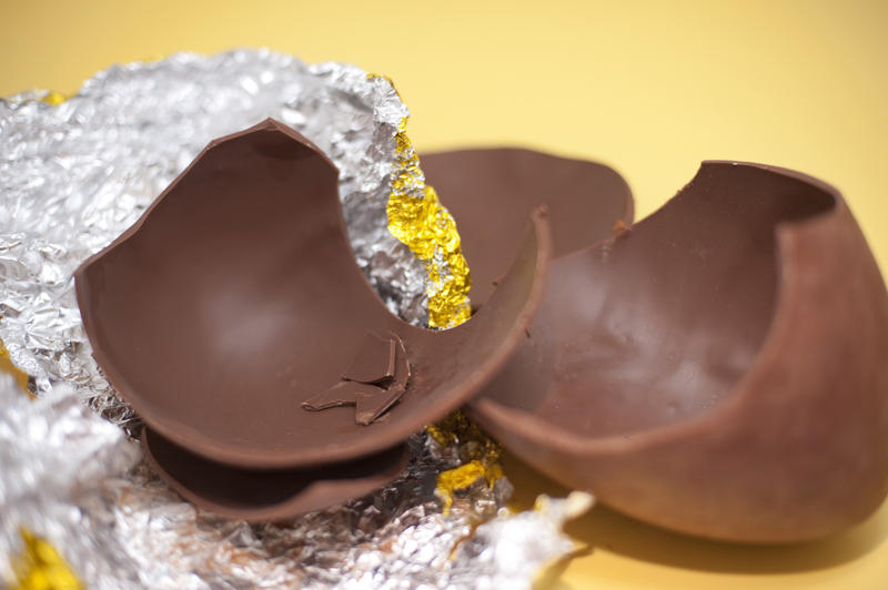 Broken chocolate Easter Egg pieces with the foil wrapper on a yellow background