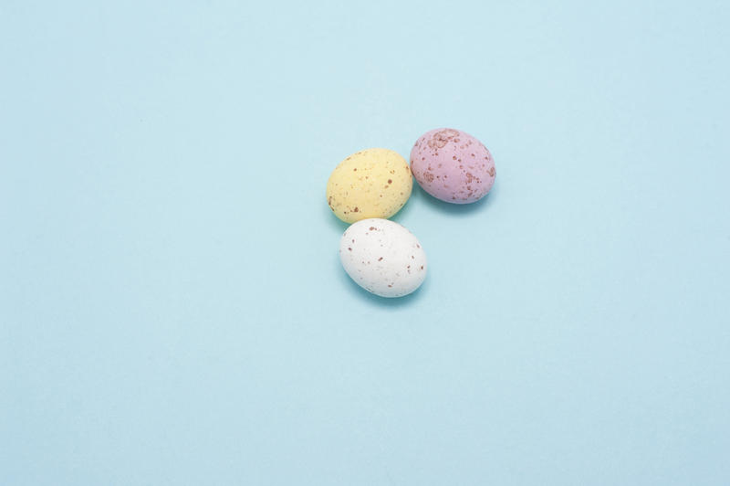 Three small sugared chocolate Mini Eggs on a blue background with plenty of copyspace for Easter