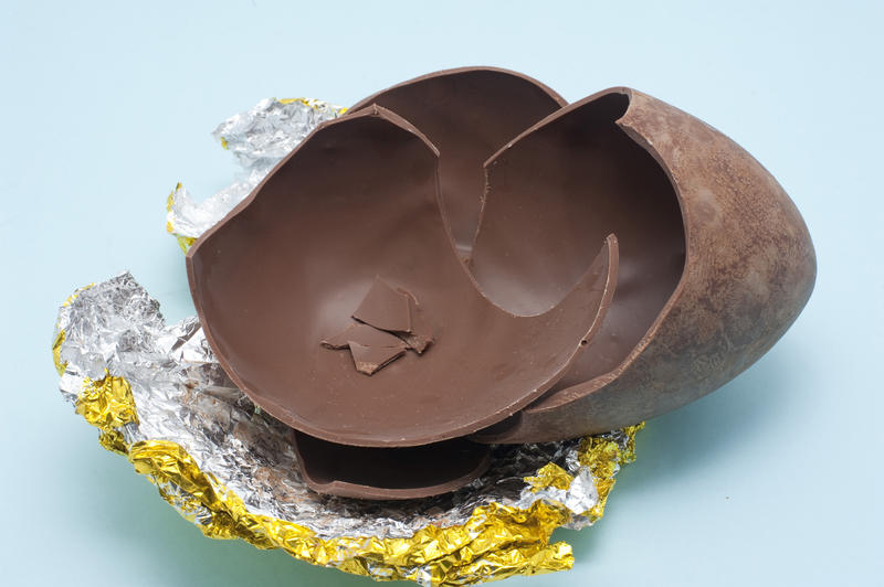 The cracked pieces of a chocolate Easter Egg lying on the silvered foil wrapper.