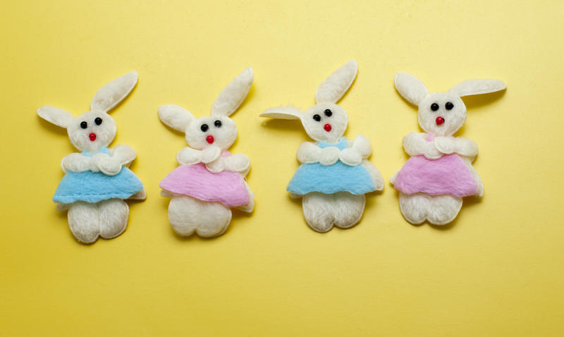 Four decorative needlework Easter Bunnies of soft felt wearing pink and blue garments on a yellow background