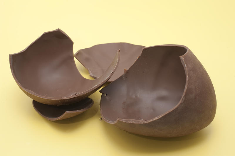 Pieces of a large broken chocolate Easter Egg on a yellow background