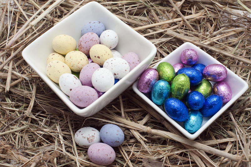 Two square ceramic dishes filled with sugared candy and foil wrapped colourful mini Easter Eggs on a straw background