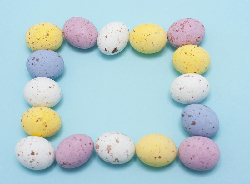 Mini Egg Easter Frame of speckled candy Easter eggs arranged in a square on a turquoise blue background