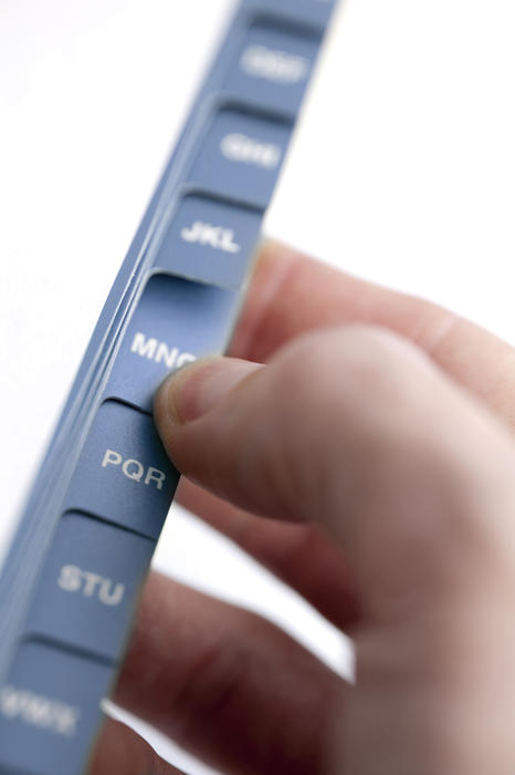Male fingers searching an alphabetical tabbed index on an address book for an entry and information