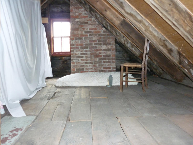 Interior of an attic roof space with a timber floor and wooden roof trusses with a single old chair under a window