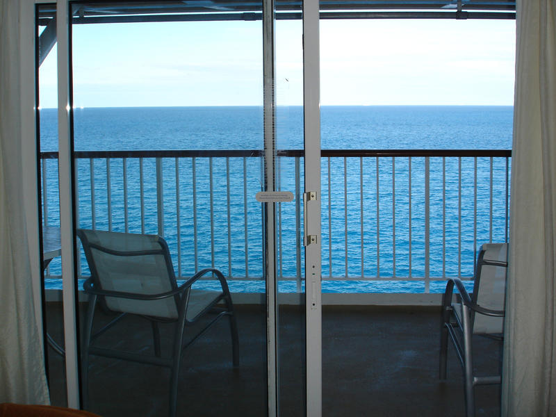 View though glass doors of two empty chairs on a balcony overlooking the ocean