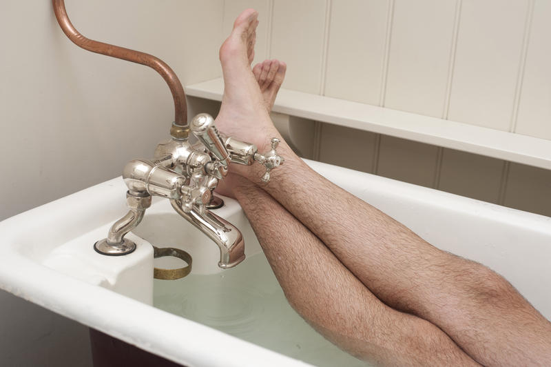 Man enjoying a hot relaxing bath in a vintage bathtub with his feet resting comfortably on the rim