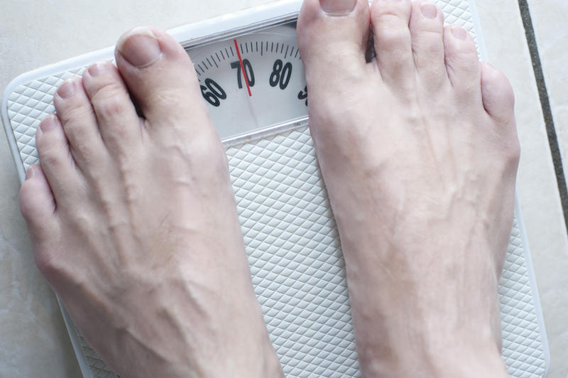 Man standing barefoot on a bathroom scale keeping a record of his weight to ensure that his weight remains stable