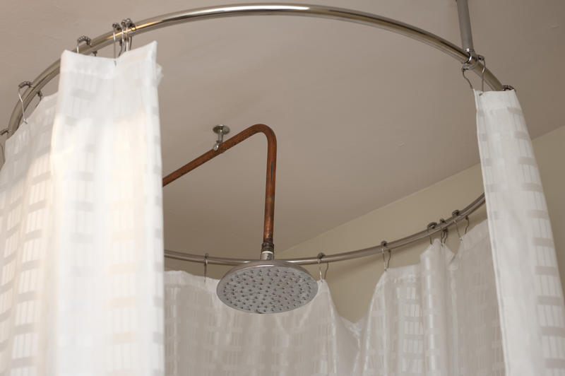 Compact round bathrrom shower cubicle with a large metal shower head and surrounded by a curtain on a circular rail