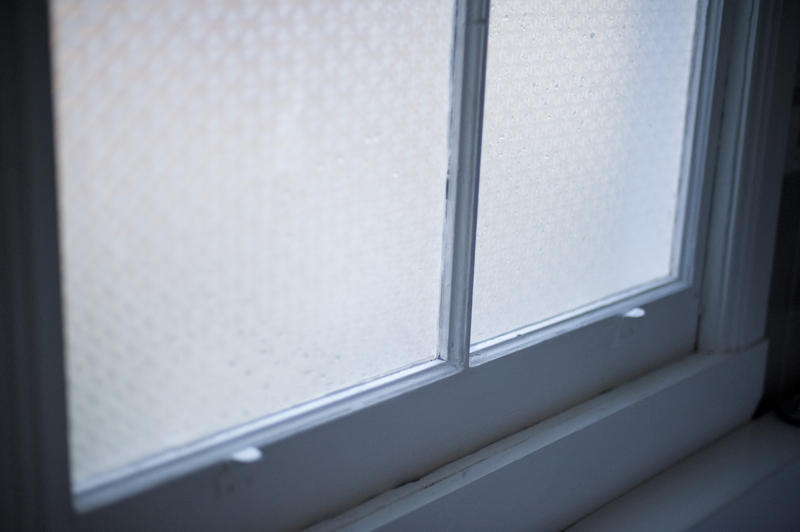 Detail of a bathroom window with opaque patterned glass to ensure privacy and a sash frame