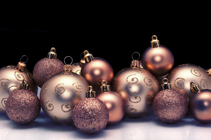 Arrangement of gold Christmas baubles of different sizes, textures and patterns against a dark background with copyspace