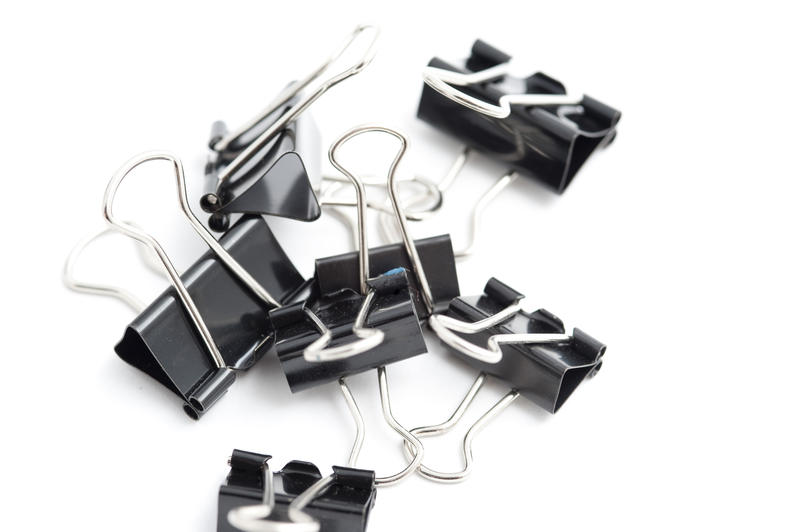 Random arrangement of binder clips on a white background for use as an office, business or banking background
