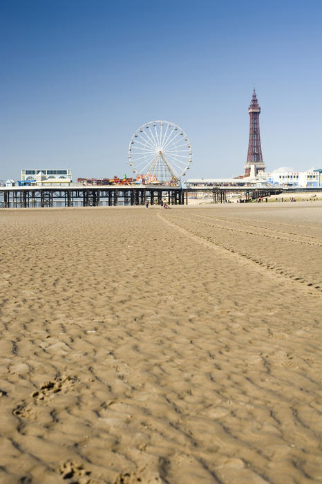 View across wet beach sand at low tide of the Blackpool Tower and Central Pier, Blackpool, England