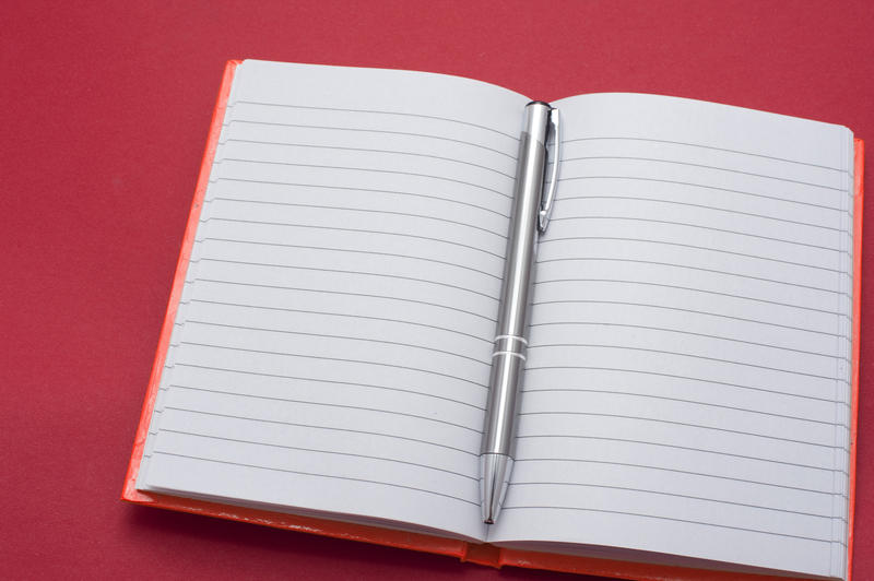 Lined blank notebook opened to the centre with a silver metallic ballpoint pen