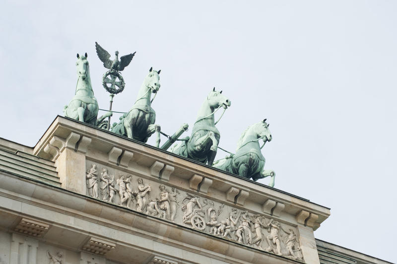 A low angle view of the bronze Quadriga on the Brandenburg Gate, Berlin showing the four prancing horses which pull Victorias chariot mounted above a decorative Roman panel on the stone facade